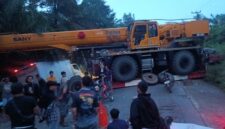 Sebuah crane melintang di badan jalan menyebabkan arus lalu lintas lumpuh total. Warga dan pengendara terlihat berkumpul saat proses evakuasi berlangsung di lokasi kejadian.