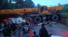 Sebuah crane melintang di badan jalan menyebabkan arus lalu lintas lumpuh total. Warga dan pengendara terlihat berkumpul saat proses evakuasi berlangsung di lokasi kejadian.