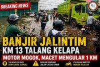 Polisi mengatur arus lalu lintas di tengah banjir Jalintim KM 13 Talang Kelapa, Banyuasin. Genangan air menyebabkan motor mogok dan kemacetan panjang.